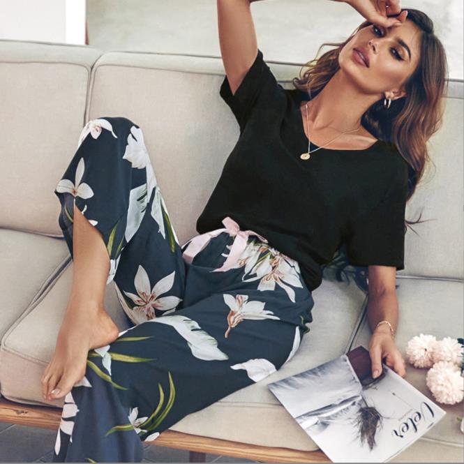 Frau in schwarzem T-Shirt und geblümter Hose auf Sofa, modisch, lässig, Wohnzimmer.