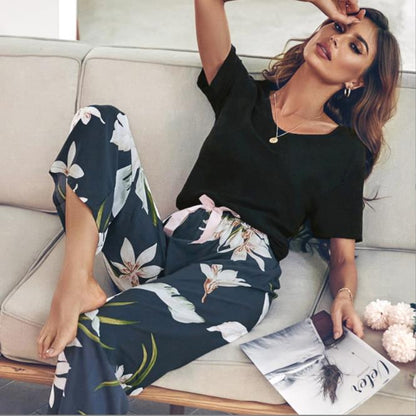 Frau in schwarzem T-Shirt und geblümter Hose auf Sofa, modisch, lässig, Wohnzimmer.