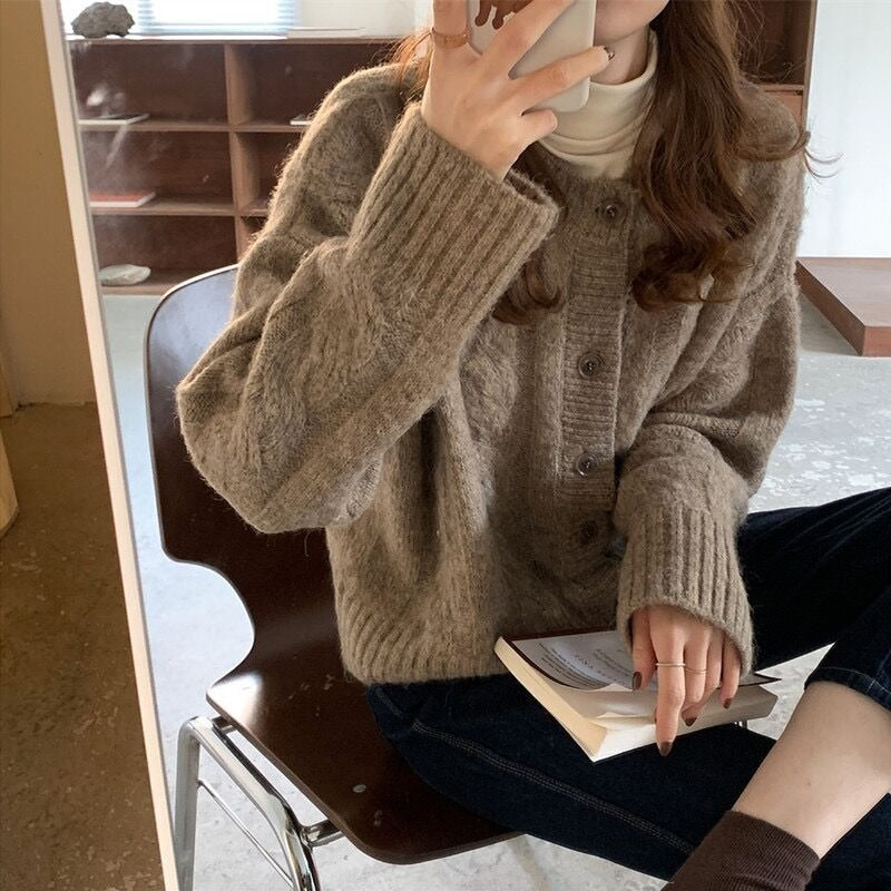 Frau in beigem Strickpullover, hält Buch, sitzt auf Stuhl, gemütliche Herbstmode.