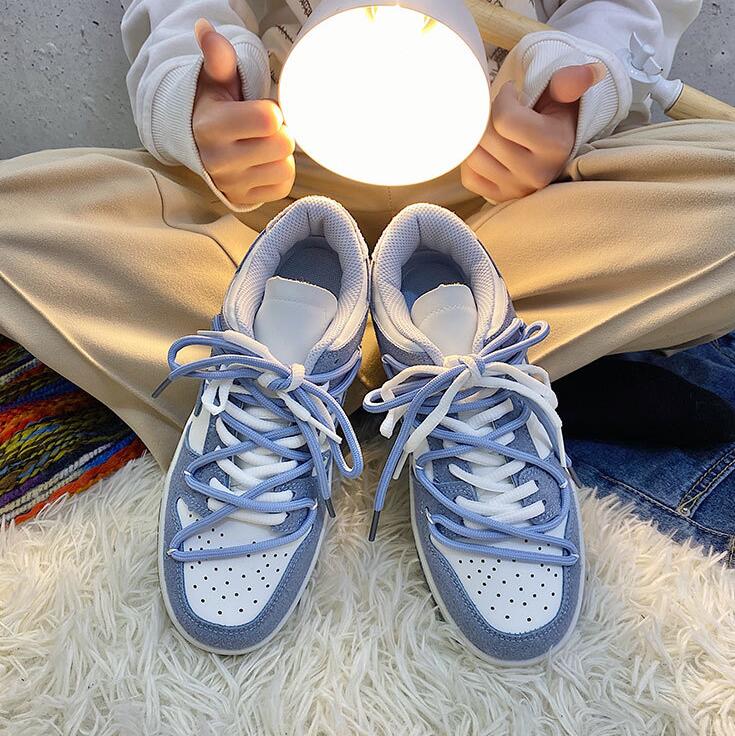 Weiße und blaue Sneaker mit Schnürsenkeln auf Teppich, moderne Freizeitschuhe.