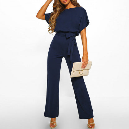Frau in dunkelblauem Jumpsuit mit Gürtel, hält beige Clutch, elegante Mode.
