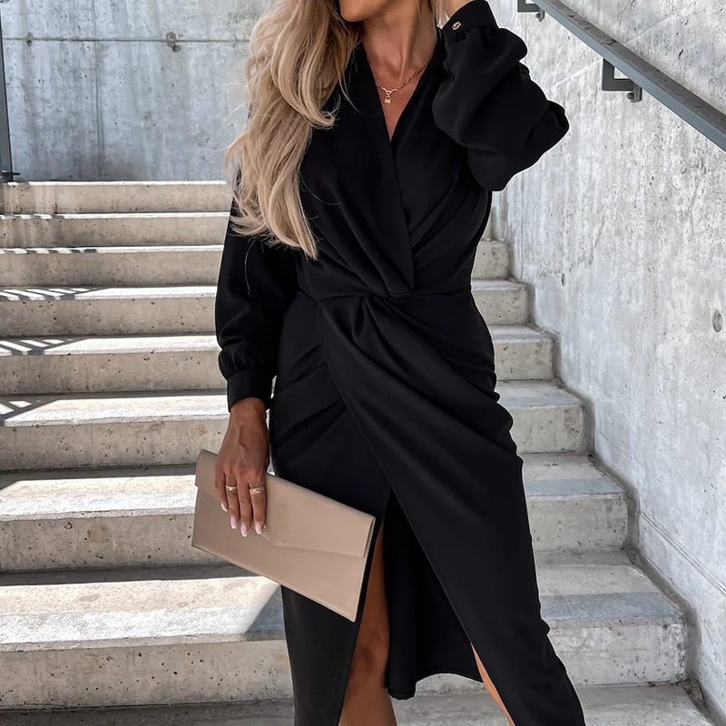 Frau in elegantem schwarzem Wickelkleid mit beigem Clutch auf Betontreppe.