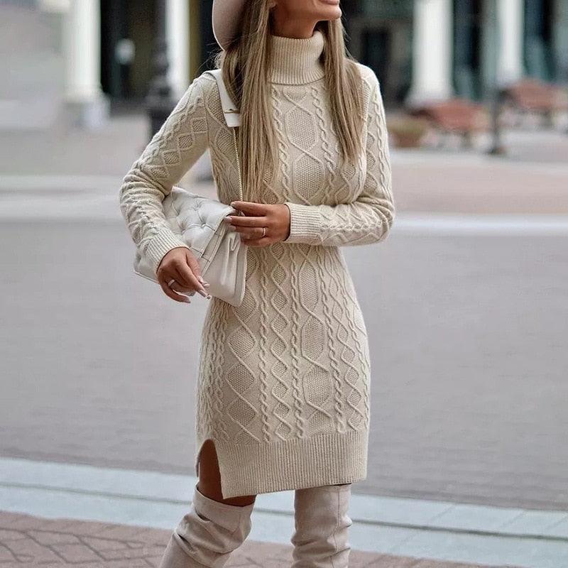 Frau in cremefarbenem Strickkleid mit Rollkragen, hält weiße Tasche, trägt Hut und Stiefel.