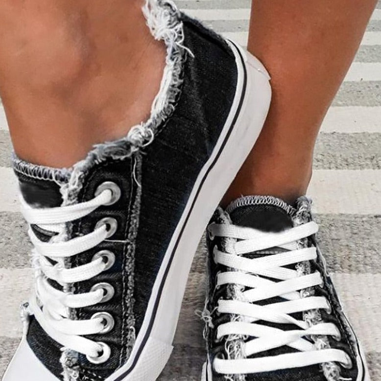 Schwarze Canvas-Sneaker mit weißen Schnürsenkeln und abgenutztem Saum auf gestreiftem Teppich.