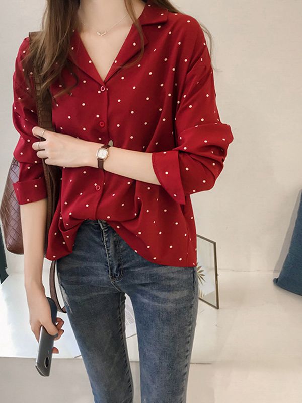 Frau in roter gepunkteter Bluse und Jeans, hält Smartphone, modisch, lässiger Look.