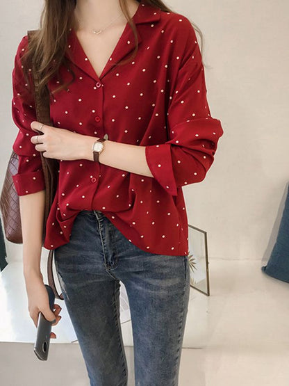 Frau in roter gepunkteter Bluse und Jeans, hält Smartphone, modisch, lässiger Look.