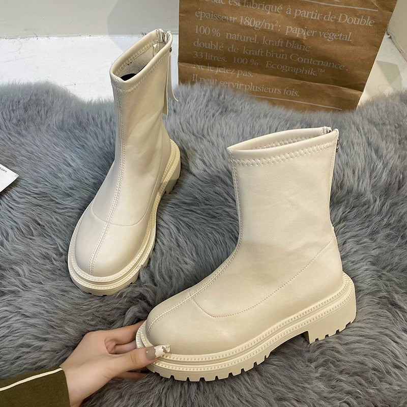 Beige Damenstiefel aus Leder mit Reißverschluss, klobige Sohle, auf grauem Teppich.