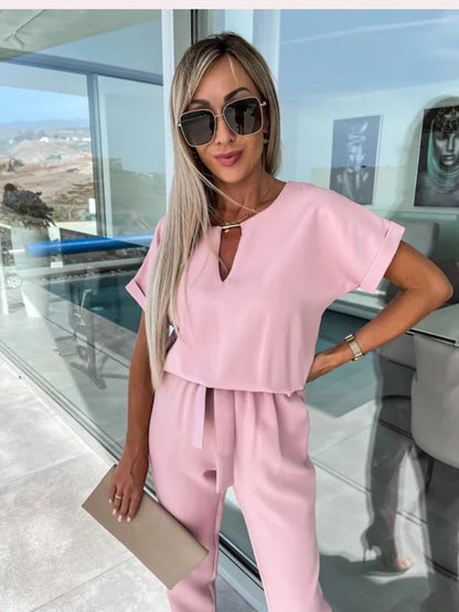 Frau in rosa Jumpsuit, Sonnenbrille, blonden Haaren, hält beigen Umschlag, moderne Terrasse.