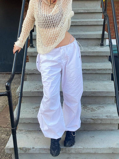 Frau in weißer Netzstrickpullover und weißer Hose auf Treppe, modische Freizeitkleidung.