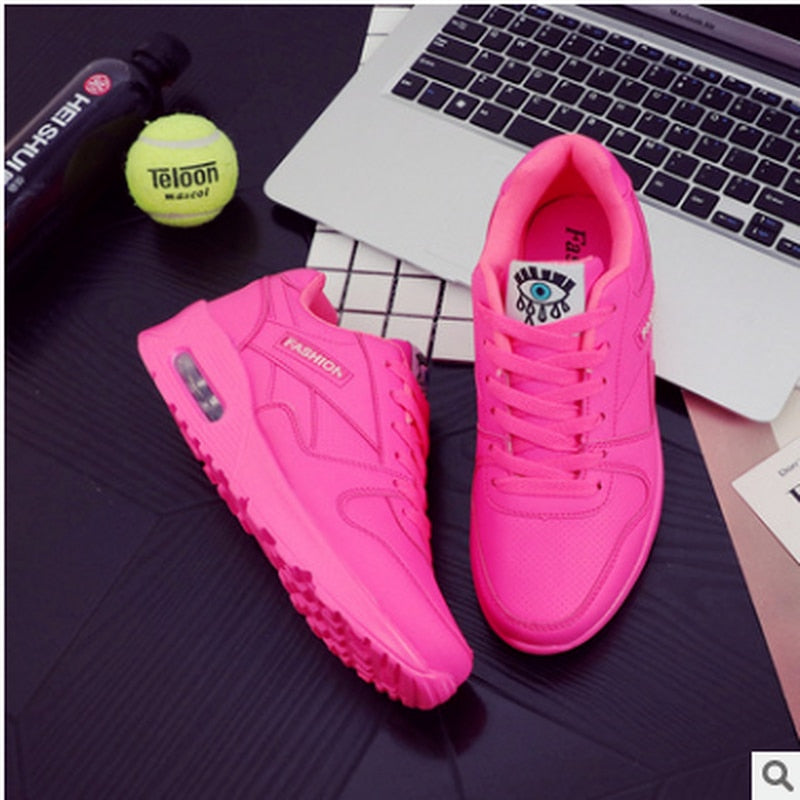 Leuchtend pinke Sportschuhe auf Laptop, Tennisball und Wasserflasche, modisch und auffällig.