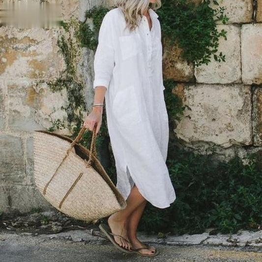 Frau in weißem Leinenkleid mit Strohtasche vor Steinmauer, Sommermode, lässiger Stil.