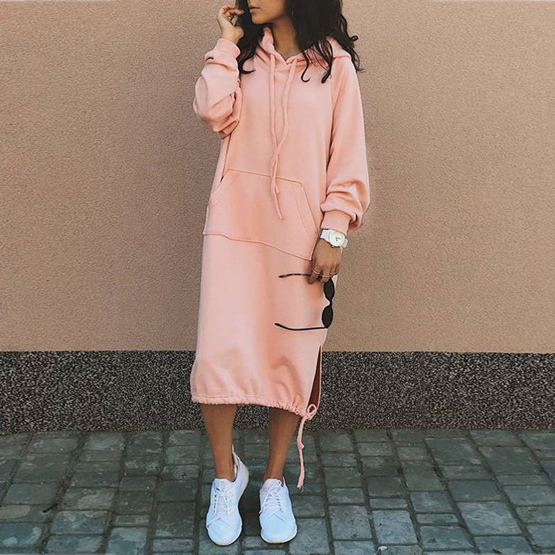 Frau in rosa Kapuzenkleid, weiße Sneaker, Sonnenbrille, lässiger Streetstyle-Look.