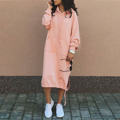 Frau in rosa Kapuzenkleid, weiße Sneaker, Sonnenbrille, lässiger Streetstyle-Look.