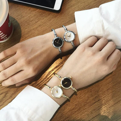 Zwei elegante Armbanduhren, schwarz und weiß, an Handgelenken, auf Holztisch, modisch, Damen.