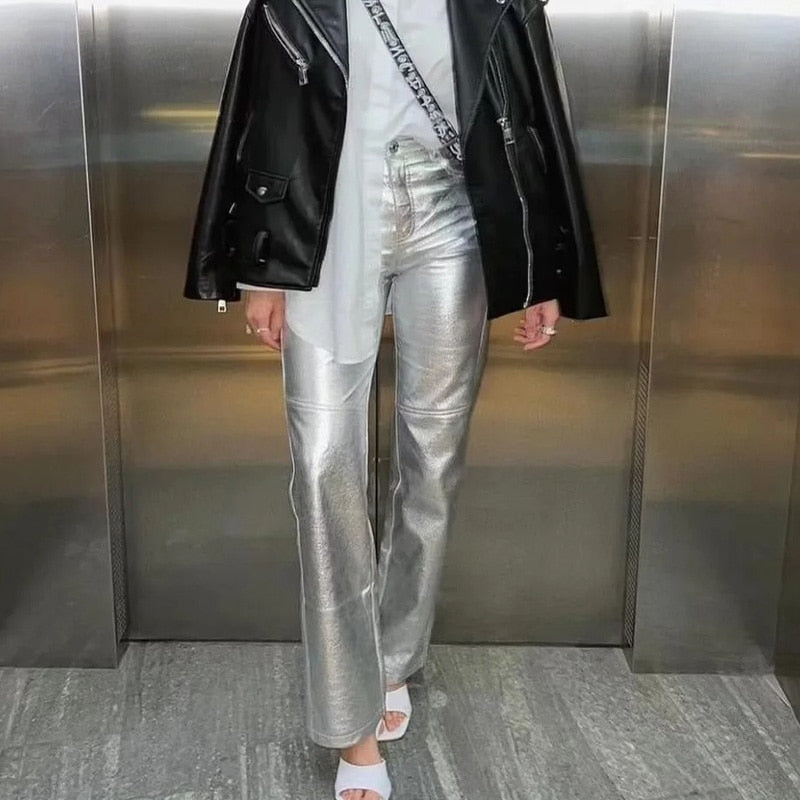 Frau in silberner Lederhose, schwarzer Lederjacke, weißem Top und Sandalen in Aufzug.