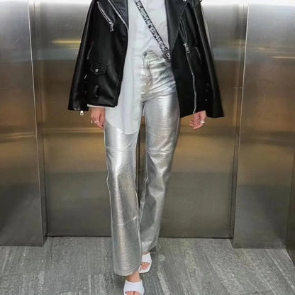 Frau in silberner Lederhose, schwarzer Lederjacke, weißem Top und Sandalen in Aufzug.