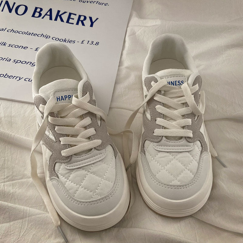 Weiße Sneaker mit grauen Details, gestepptem Muster, Schnürsenkeln, auf weißem Hintergrund.