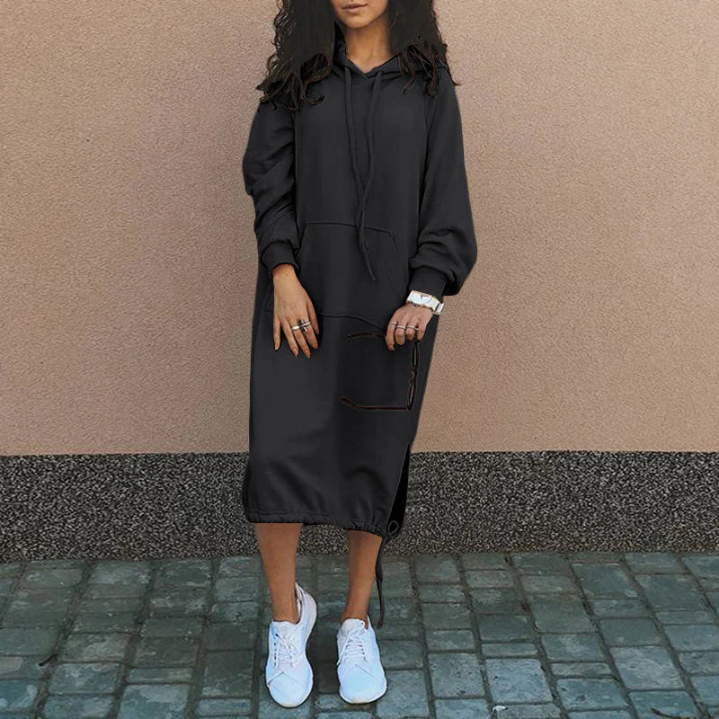 Frau in schwarzem Hoodie-Kleid, lässig, mit weißen Sneakers, urbaner Stil.