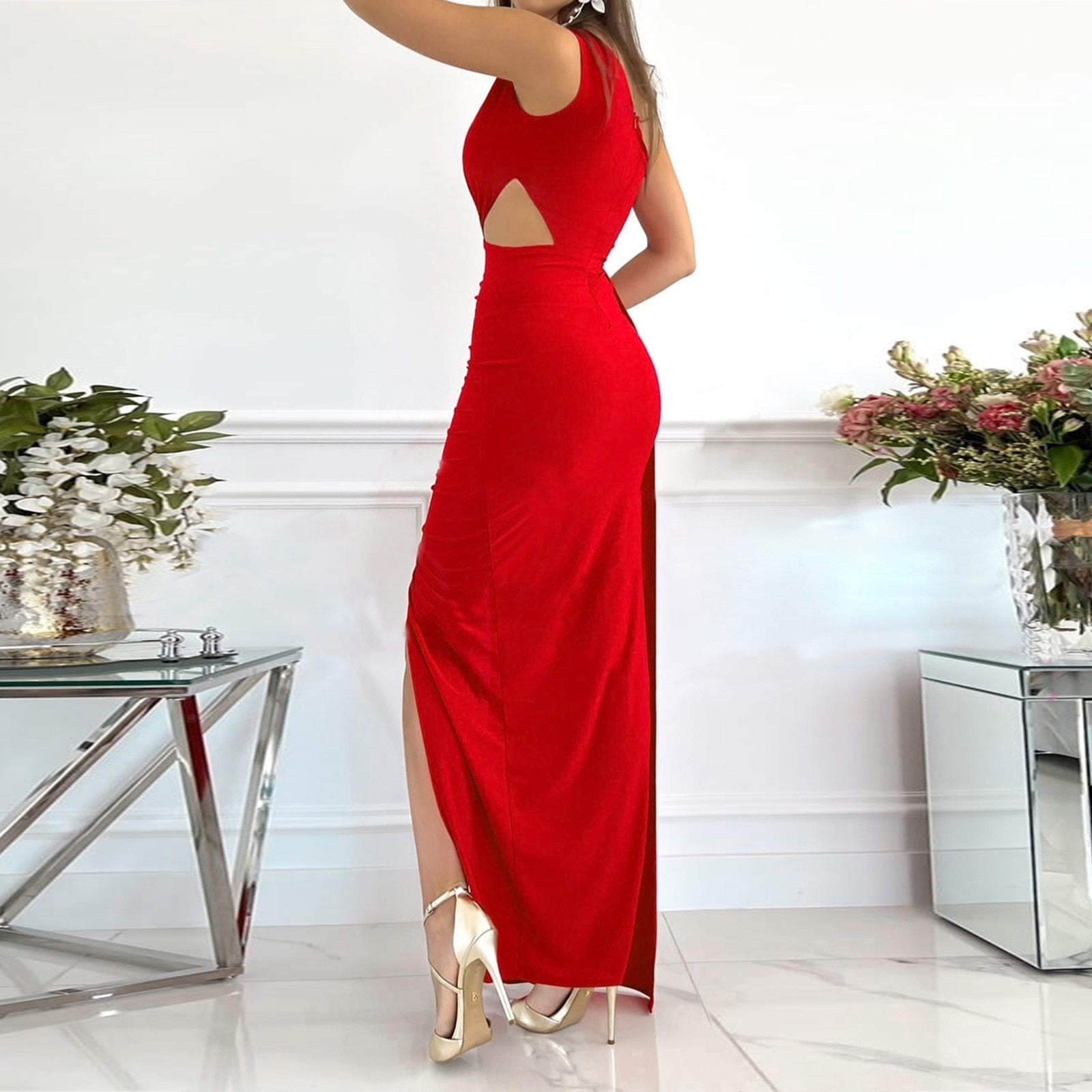 Frau im eleganten roten Abendkleid mit Rückenausschnitt, Blumenarrangement im Hintergrund.