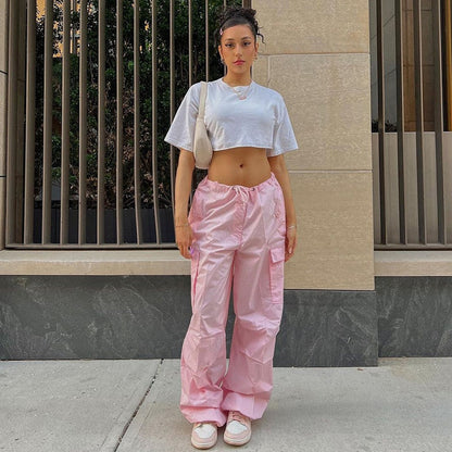Frau in weißem Crop-Top und rosa Cargo-Hose, lässiger Streetwear-Look, urbaner Hintergrund.