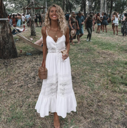 Frau im weißen Sommerkleid mit Spitze, hält Getränk, Outdoor-Event, modisch, elegant.