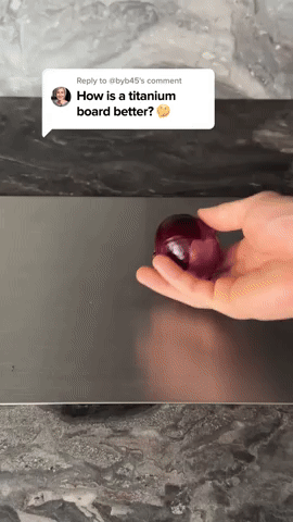 Hand håller en röd lök över en slät, mörkgrå skärbräda på en marmorbänk, bildruta från en video. 5