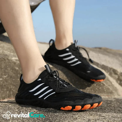 Schwarze Sportschuhe mit weißen Streifen und orangefarbener Sohle auf Felsen.