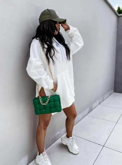 Frau in weißem Hoodie, grüner Tasche, Basecap und Sneakers, lässiger Streetstyle-Look.