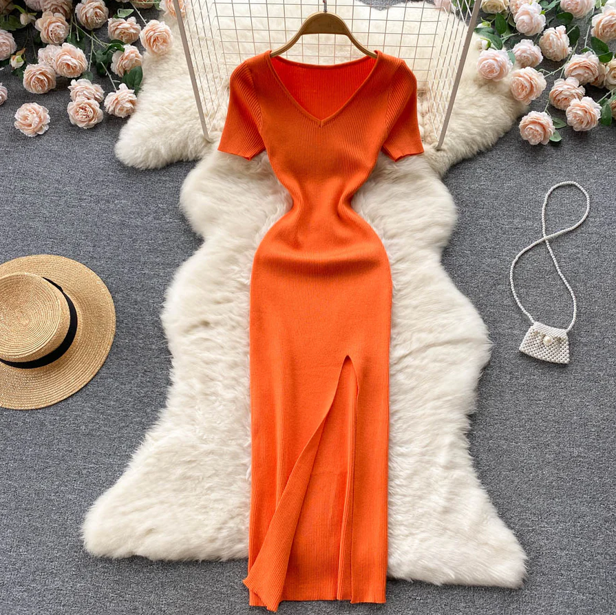 Orangefarbenes Strickkleid mit V-Ausschnitt und Schlitz, elegant, auf weißem Fellteppich.