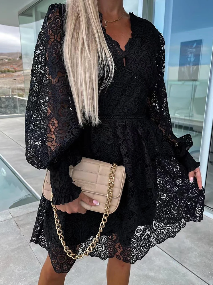 Frau in schwarzem Spitzenkleid mit beiger Handtasche und goldener Kette auf Balkon.