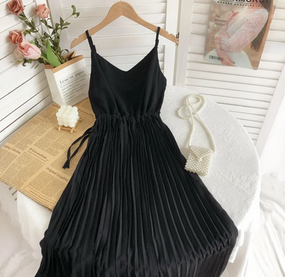 Schwarzes, ärmelloses Plisseekleid auf Tisch mit Perlenhandtasche und Rosen im Hintergrund.