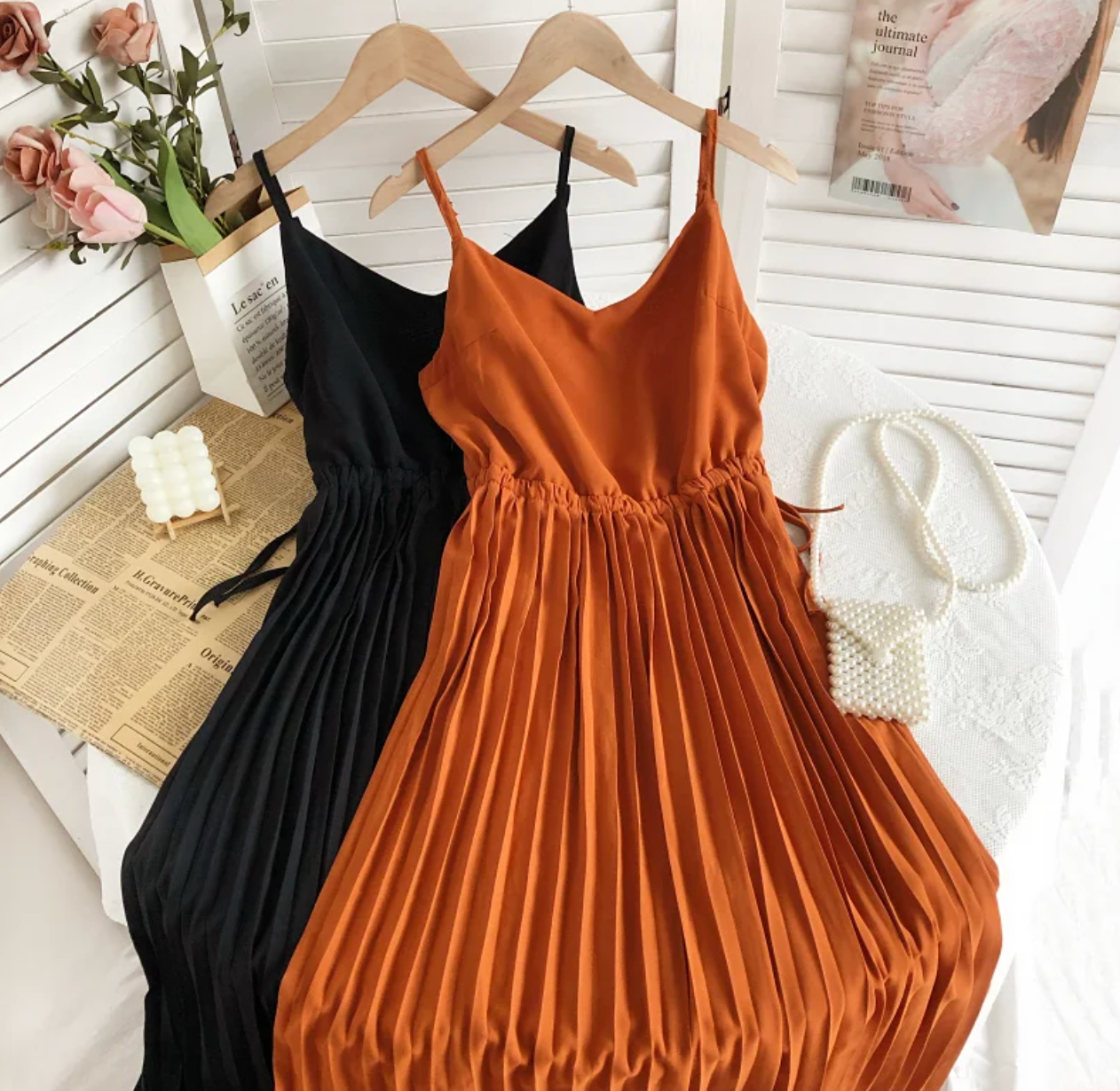 Zwei plissierte Sommerkleider, schwarz und orange, aus Satin auf Holzkleiderbügeln.