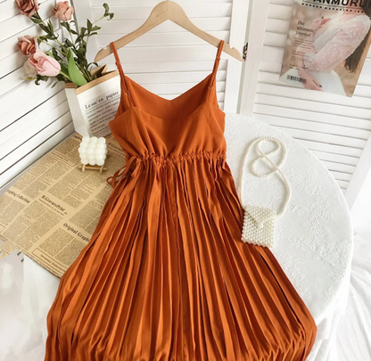 Orangefarbenes, plissiertes Sommerkleid aus Satin auf weißem Tisch mit Perlenhandtasche.