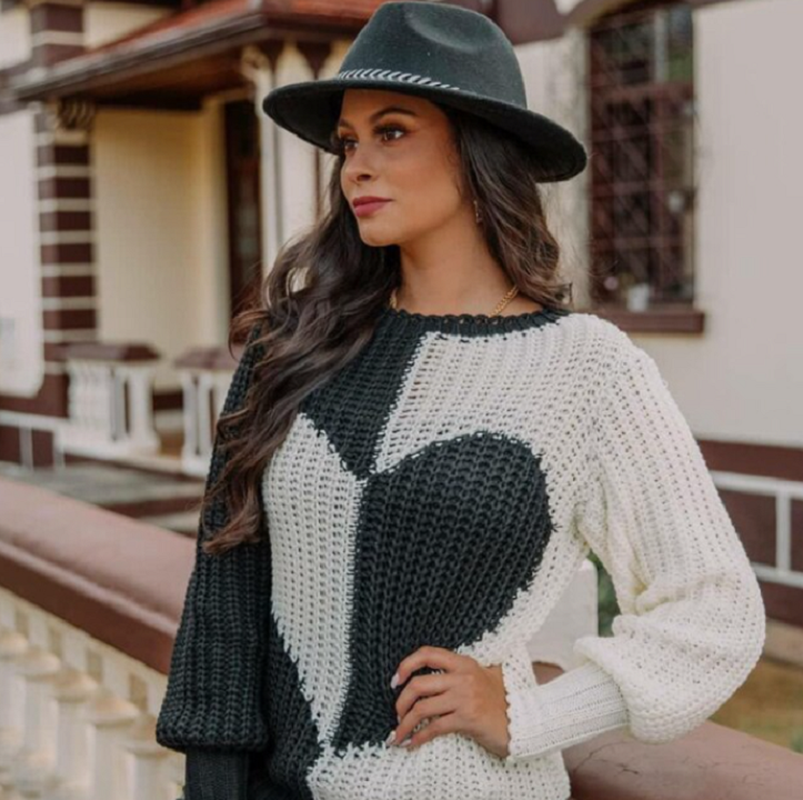Frau mit schwarz-weißem Herzpullover und schwarzem Hut vor einem Gebäude.