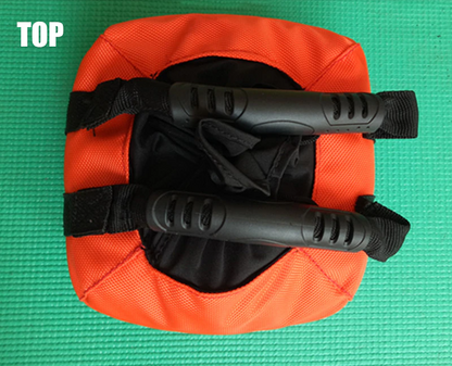 Orangefarbener Sandsack mit schwarzen Griffen auf grünem Hintergrund, Fitnesszubehör.