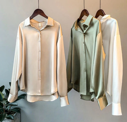 Drei seidene Blusen in Beige, Grün und Weiß auf Kleiderbügeln, elegante Damenmode.