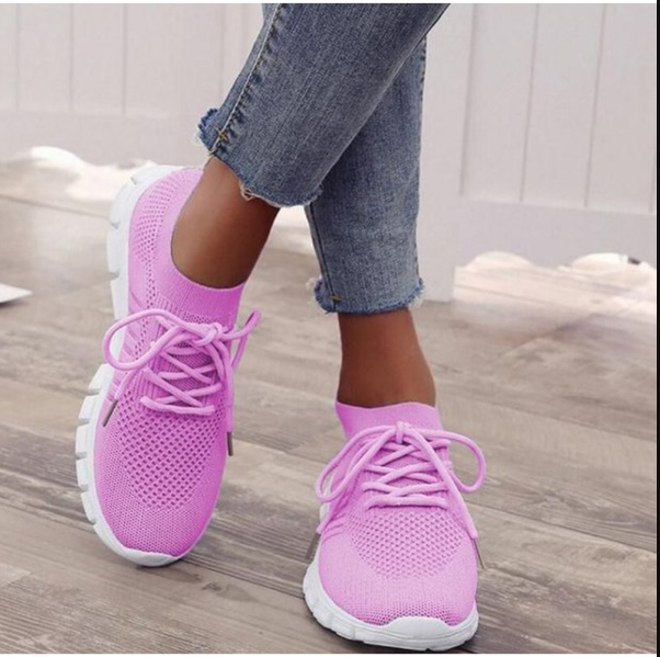 Frau trägt pinke Sneaker, atmungsaktiv, sportlich, mit weißen Sohlen, Jeans, Holzboden.