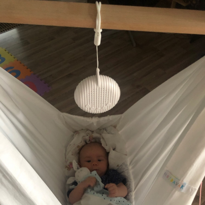 Kleinkind in weißer Babyhängematte mit Spielzeug, Holzrahmen, gemütliches Kinderzimmer.