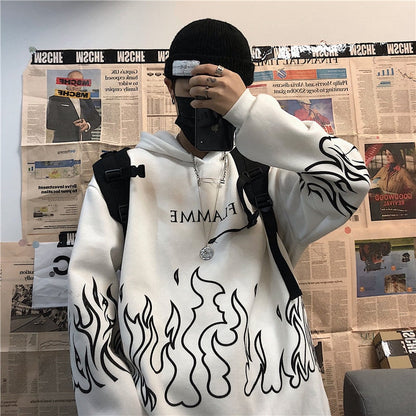 Person in weißem Hoodie mit Flammenmuster, schwarzer Mütze, Smartphone, vor Zeitungswand.