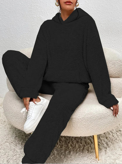 Frau in schwarzem Fleece-Hoodie und Jogginghose, weiße Sneaker, sitzt auf modernem Sessel.