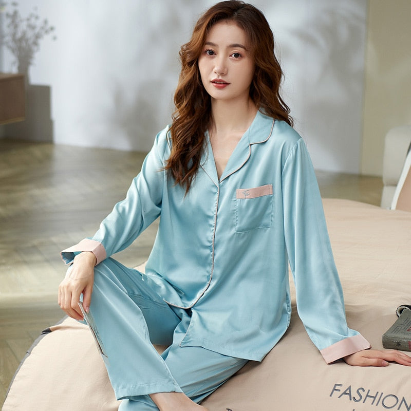 Frau in hellblauem Seidenpyjama sitzt auf Bett, elegantes Nachtwäsche-Design.