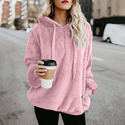 Frau in rosa Fleece-Hoodie hält Kaffeebecher, lässige Straßenmode, Herbstbekleidung.