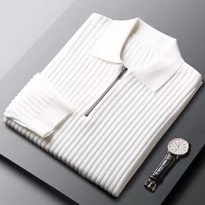 Zusammengelegter weißer Strickpullover mit Reißverschluss und Armbanduhr auf grauem Hintergrund.