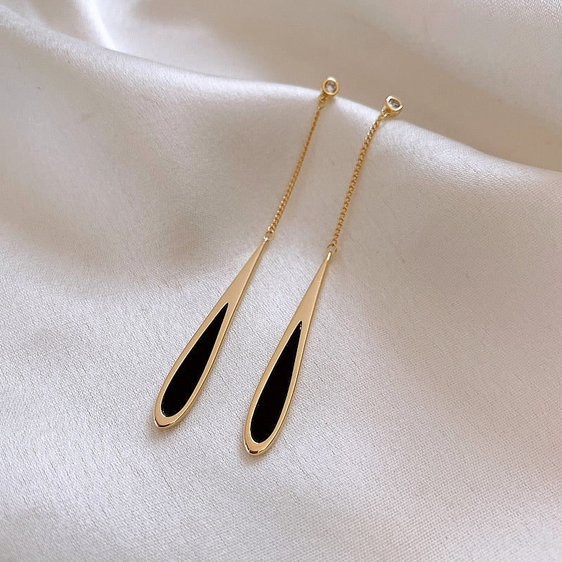 Goldene Ohrringe mit schwarzem Tropfen-Design auf weißem Stoff, eleganter Schmuck.