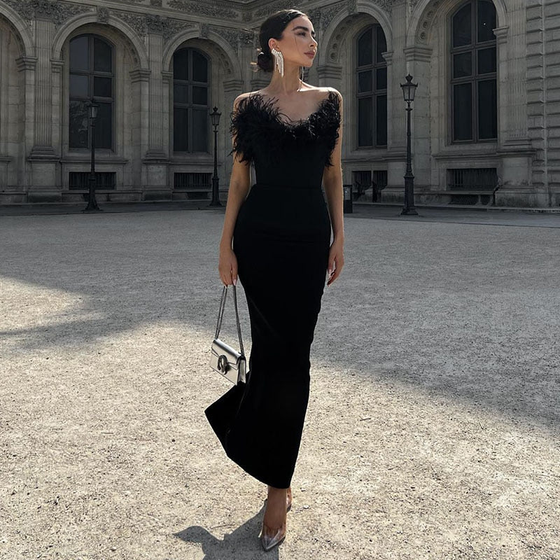Frau in elegantem schwarzem Abendkleid mit Federn, steht vor historischer Architektur.