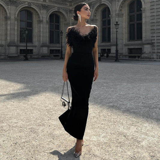 Frau in elegantem schwarzem Abendkleid mit Federn, steht vor historischer Architektur.