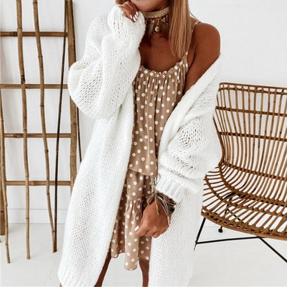Frau in weißem Strickcardigan und gepunktetem Kleid vor Bambusdekor.
