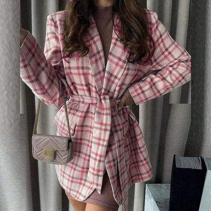 Frau in rosa kariertem Mantel mit Gürtel, braunes Kleid, kleine Umhängetasche, modisch.