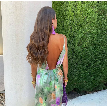 Frau im rückenfreien, bunten Sommerkleid vor grüner Hecke, lange braune Haare, lila Ohrringe.