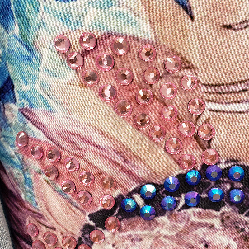 Nahaufnahme von rosa und blauen Strasssteinen auf bedrucktem Stoff, glitzerndes Design.
